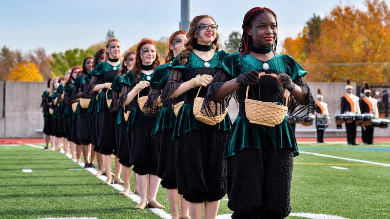 Color guard performers in coordinated green and black costumes on a football field.