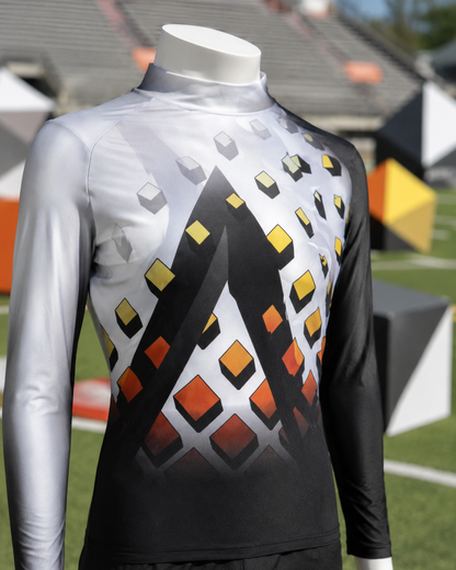 Close-up of a black, white, orange, and yellow marching band performance top with a geometric cube print, displayed on a football field with matching cube-shaped field props.