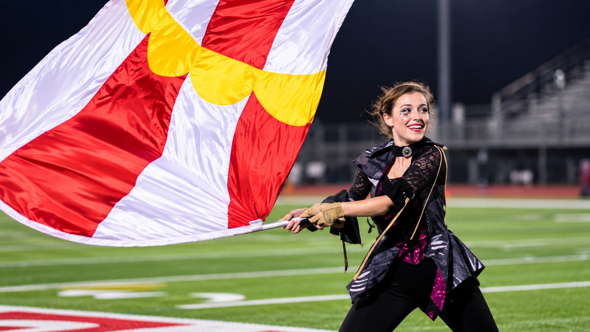Color guard performer presenting a large red, white, and yellow flag on a football field.